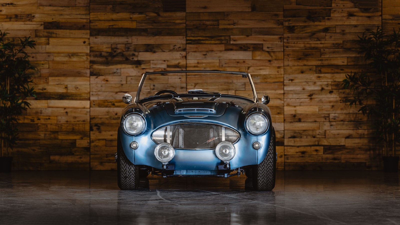 Blue Sebring 3000e roadster in front of a wooden workshop wall